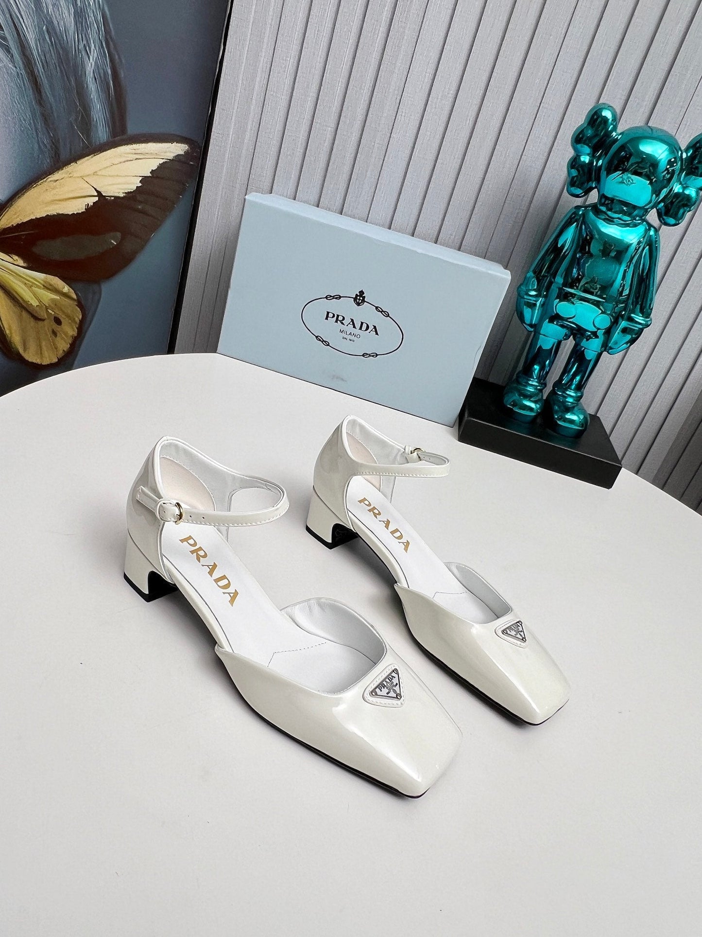 ЖІНОЧІ ТУФЛІ PRADA 26S НА КАБЛУКУ 40 ММ З РЕМІНЦЕМ НА ЩИКОЛОТЦІ З БІЛОЇ ЛАКОВАНОЇ ШКІРИ ТЕЛЯТИ З ЛОГОТИПОМ У ВИГЛЯДІ ТРИКУТНИКА