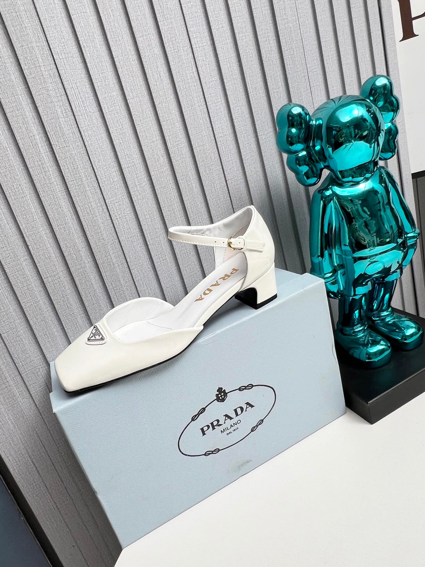 ЖІНОЧІ ТУФЛІ PRADA 26S НА КАБЛУКУ 40 ММ З РЕМІНЦЕМ НА ЩИКОЛОТЦІ З БІЛОЇ ЛАКОВАНОЇ ШКІРИ ТЕЛЯТИ З ЛОГОТИПОМ У ВИГЛЯДІ ТРИКУТНИКА
