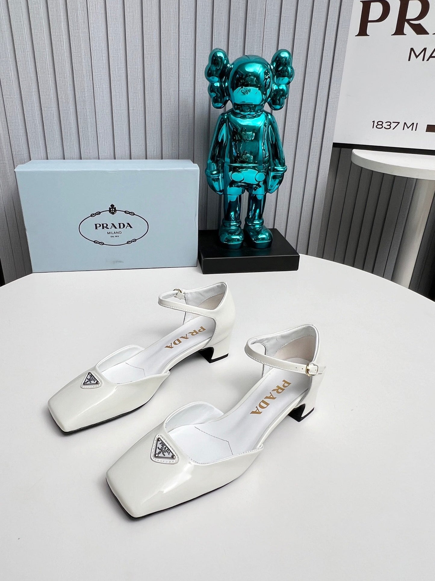 ЖІНОЧІ ТУФЛІ PRADA 26S НА КАБЛУКУ 40 ММ З РЕМІНЦЕМ НА ЩИКОЛОТЦІ З БІЛОЇ ЛАКОВАНОЇ ШКІРИ ТЕЛЯТИ З ЛОГОТИПОМ У ВИГЛЯДІ ТРИКУТНИКА